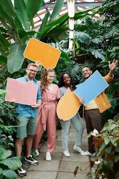 Cheerful group of friends holding colorful speech bubbles in a lush greenhouse setting.